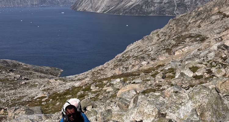 Person climbing on rocky terrain with a fjord in the background.