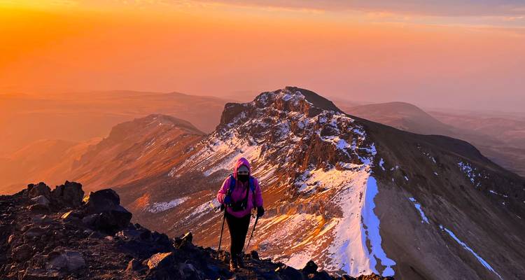 Un randonneur gravissant une montagne enneigée au coucher du soleil.