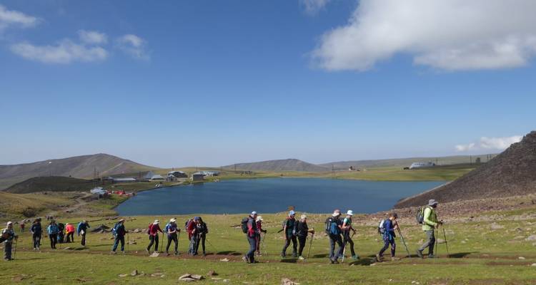 Groupe de randonneurs marchant au bord d'un lac dans une région montagneuse.