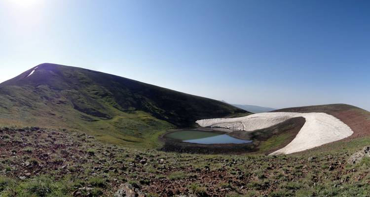 Paysage de montagne parsemé de neige avec un petit lac.