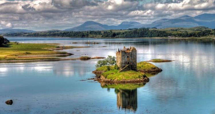 Un petit château sur une île avec un arrière-plan montagneux.