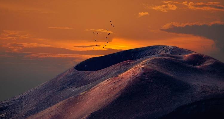 Paysage volcanique au coucher du soleil avec des silhouettes d'oiseaux.