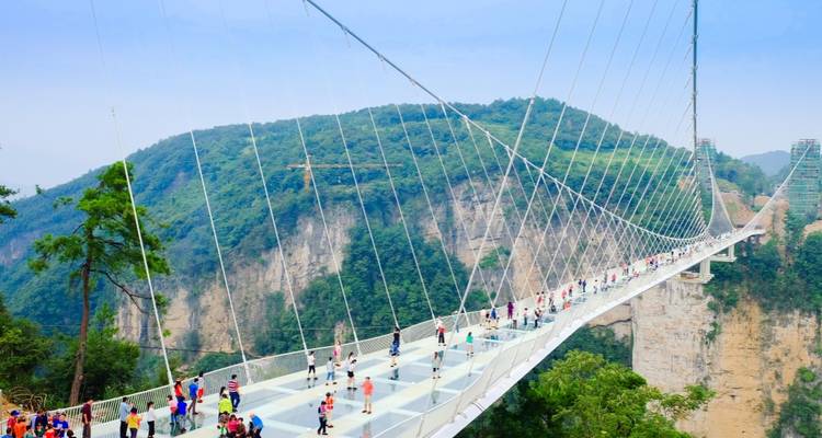 Des touristes marchant sur un pont de verre au-dessus d'un canyon.