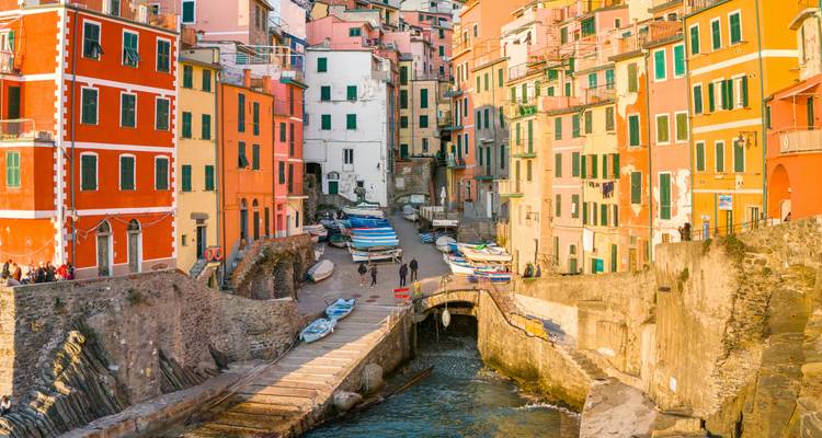 Pueblo costero de acantilado pintado de colores brillantes con botes varados en una ensenada estrecha bajo el cálido sol de la tarde.