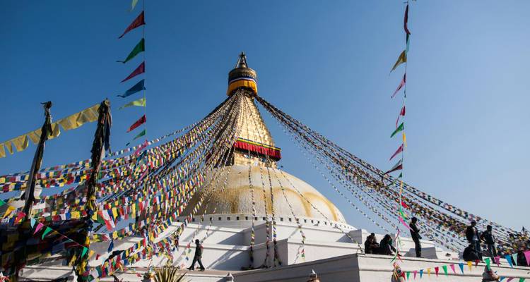 Grand stupa avec des drapeaux de prière colorés contre un ciel bleu clair.
