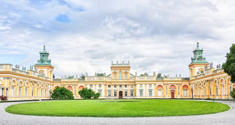 Grand palais avec une pelouse verte et un ciel nuageux.