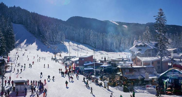 Station de ski bondée avec des gens qui skient et des montagnes enneigées.