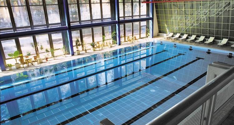 Piscine intérieure avec chaises longues près de grandes fenêtres.