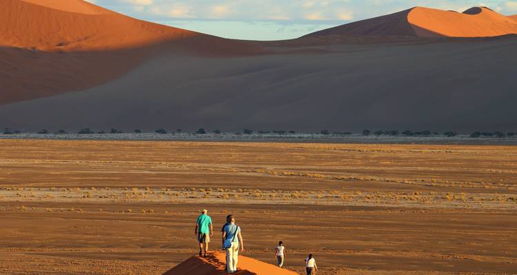 Senderistas caminando por inmensas dunas de arena roja.