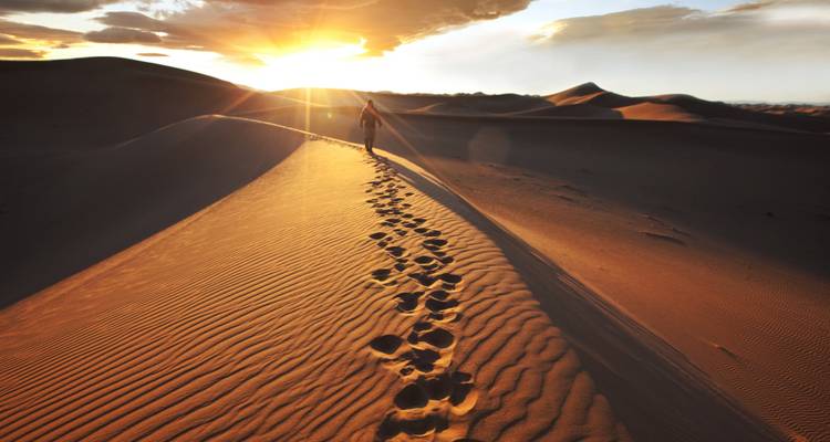 Persona caminando por las dunas de arena durante una brillante puesta de sol.