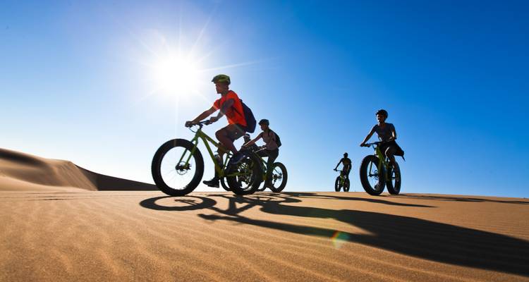 Ciclistas atravesando dunas de arena en un paisaje desértico.