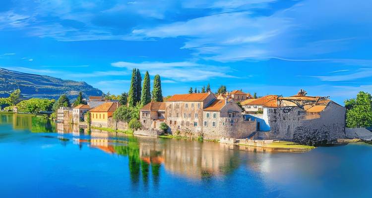 A scenic view of a small town with red-roofed buildings by a river reflecting clear blue skies.