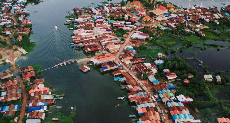 Imagen aérea de un colorido pueblo sobre pilotes que se extiende por un lago con botes y canales.