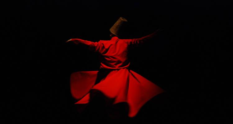 Derviche tournant en silhouette vêtu de robes rouges tournoyant sur une scène sombre