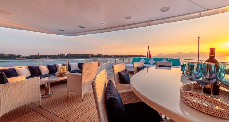 Pont spacieux de luxe d'un yacht avec sièges élégants et une table à manger donnant sur des eaux calmes de la mer au coucher du soleil