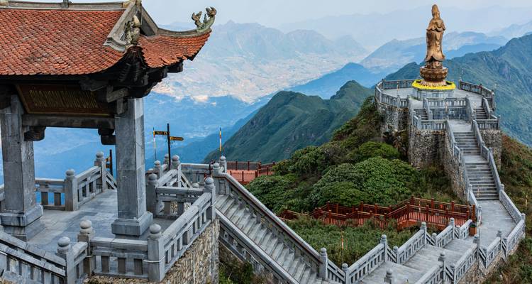 Escalinatas de piedra llevan a un Buda gigante sentado en la cima de una montaña con vistas panorámicas del valle.