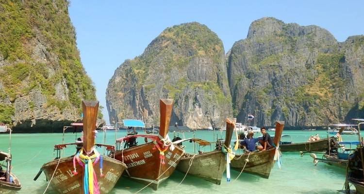 Bateaux longtail traditionnels ancrés dans une eau turquoise claire avec des falaises calcaires.