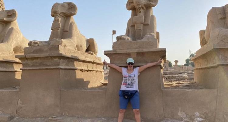 Person posing with ancient stone statues at a historical site.