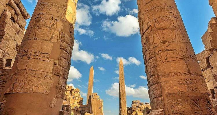 Two tall ancient obelisks framed by decorated columns under a blue sky.