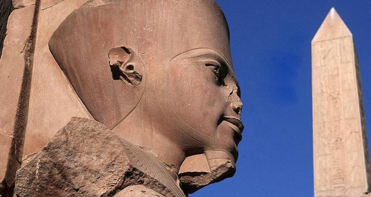 Close-up of an ancient statue and obelisk with a clear blue sky.