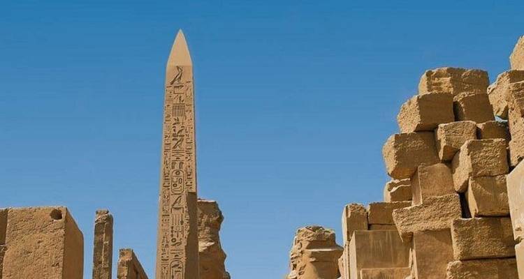 Ancient stone obelisk surrounded by ruins under a clear sky.