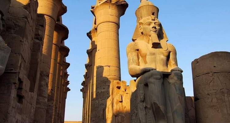 Large ancient statue surrounded by pillars and ruins.