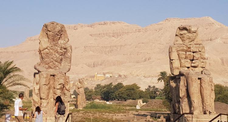 Deux statues antiques dans un paysage désertique avec des touristes à proximité.