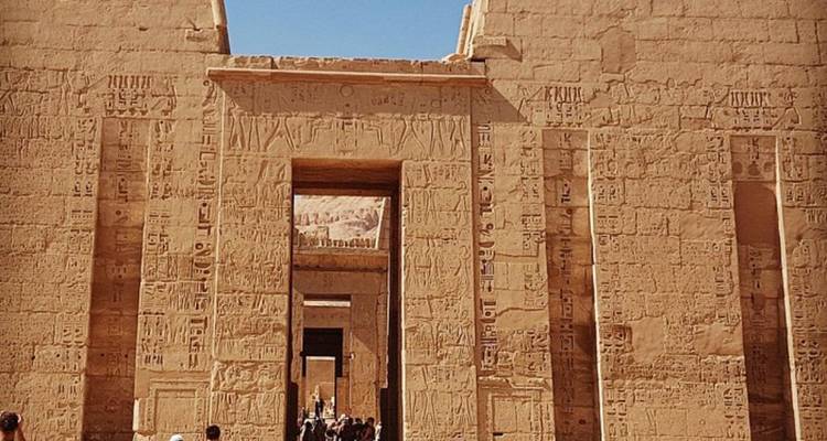 Entrée d'un temple égyptien antique avec des touristes qui explorent.