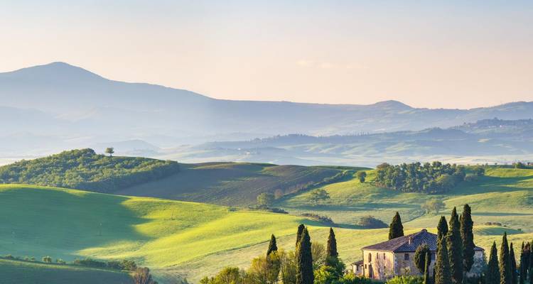Rolling hills of Tuscany with scattered trees and a farmhouse.