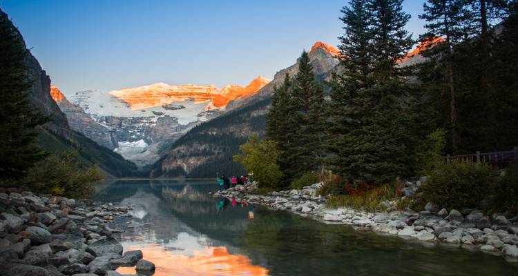 Lac avec un arrière-plan montagneux et des arbres, des gens près du rivage.