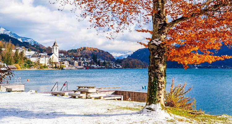Une scène sereine au bord d'un lac avec des montagnes enneigées et un feuillage d'automne.
