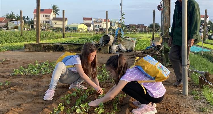 Twee kinderen die planten op een boerenveld onder toezicht van een oudere man.