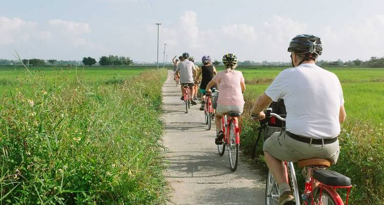 Een groep mensen die fietst op een landelijk pad met groene velden aan weerszijden.