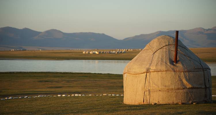 Traditionelle Jurte neben einem ruhigen See bei Sonnenuntergang.