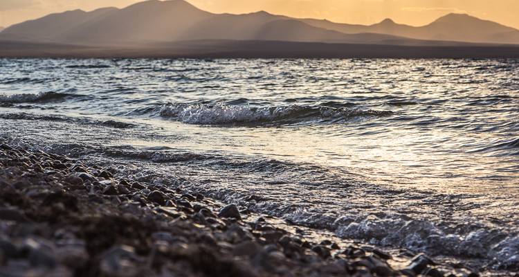 Wellen, die am Ufer brechen, mit fernen Bergen.