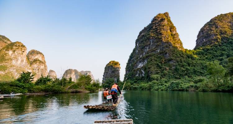 Personas navegando en balsa por un río rodeado de imponentes montañas kársticas.