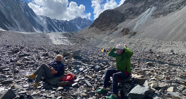Two people resting on rocky terrain with mountains.