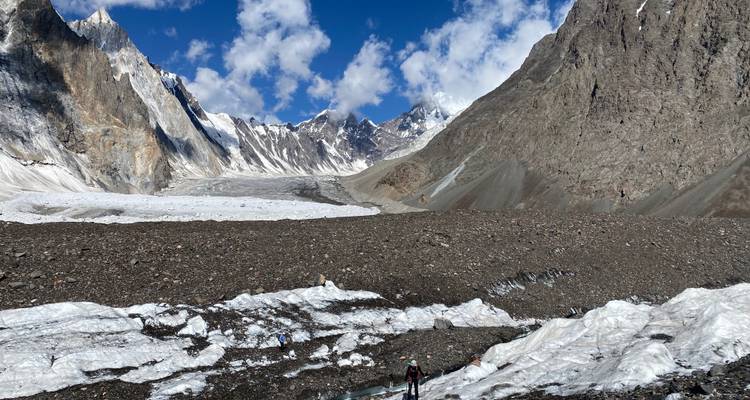Wide-angle view of hikers on a rocky glacier path with mountains.