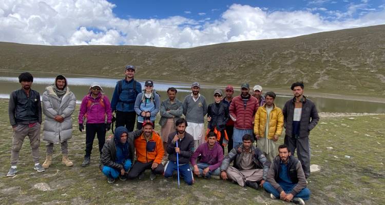 Large group of people posing by a lake with hills in the background.