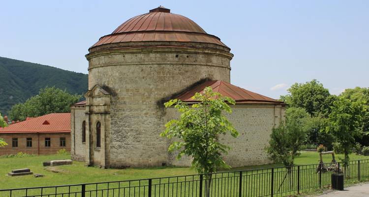 Bâtiment en pierre rond avec toit rouge dans un jardin.