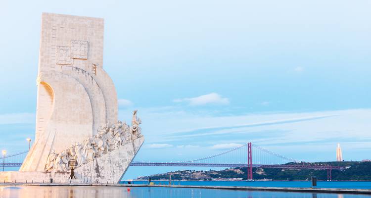 Monument aux Découvertes avec un grand pont suspendu en arrière-plan.