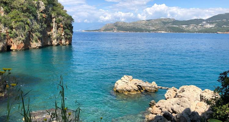 Côte rocheuse avec une eau turquoise claire et des collines au loin.