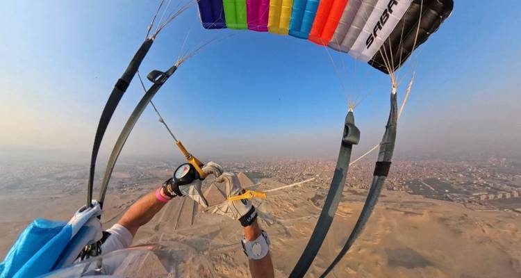 Paraglider navigeert boven piramides, stadsgezicht zichtbaar.