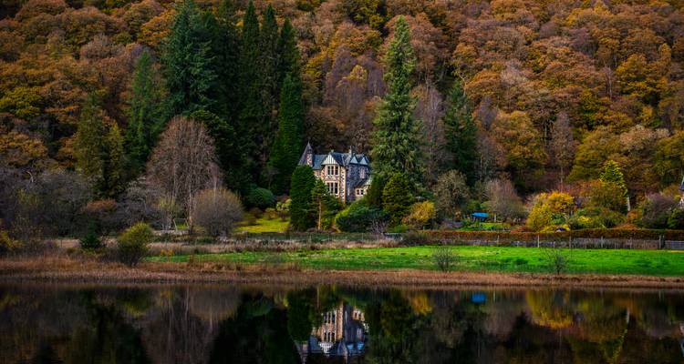 Charmante maison nichée dans une forêt aux couleurs automnales se reflétant sur l'eau.
