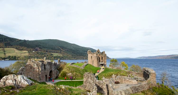 Ruines au bord d'un lac avec des collines en arrière-plan.
