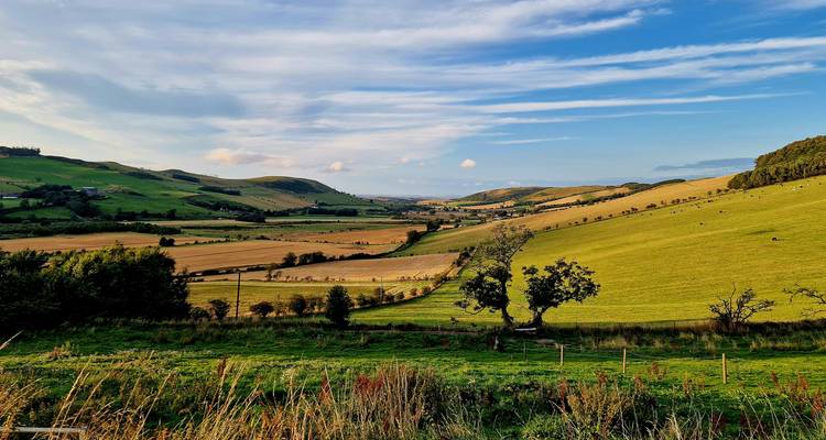 Panoramablick auf ein Tal mit Feldern unter blauem Himmel.