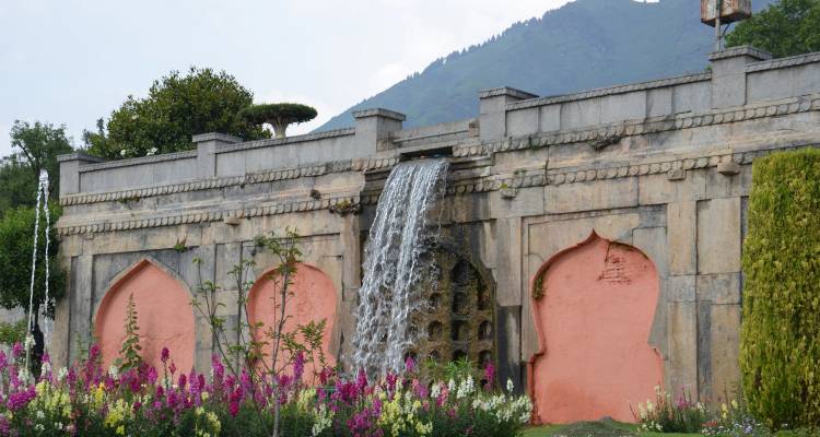 Jardín histórico con cascada y flores, arquitectura de piedra.