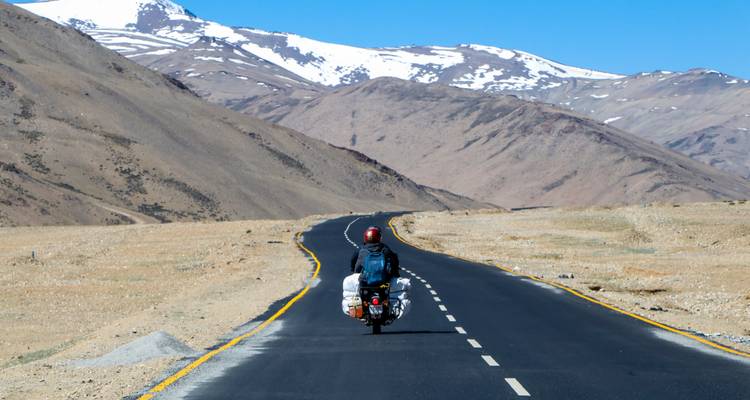 Un motociclista en una carretera con montañas de fondo.