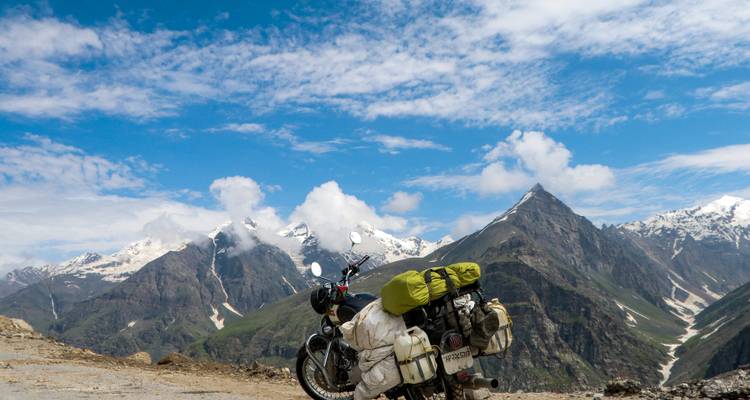 Una motocicleta estacionada con majestuosas montañas cubiertas de nieve en el fondo.