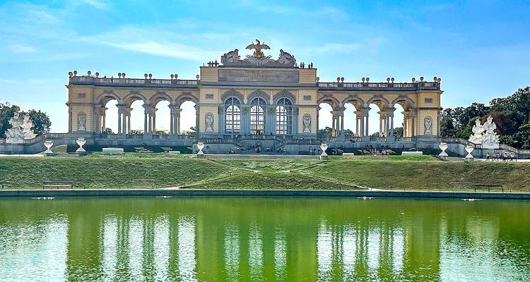 Structure historique de la Gloriette avec reflet dans l'eau, entourée d'un jardin.